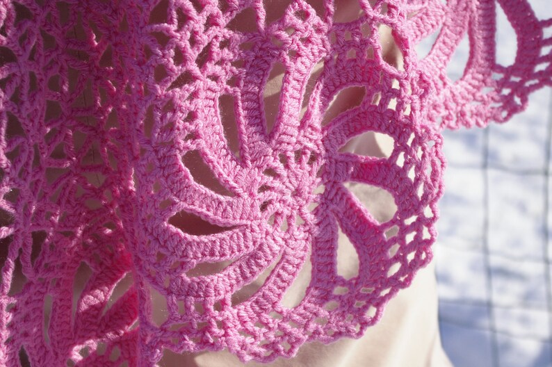 May include: Pink crocheted shawl with a delicate floral pattern. The shawl is made with a fine yarn and has a soft, airy feel.