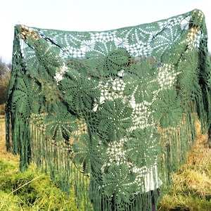 Pode incluir: Um xale de crochê verde com um padrão floral e franjas. O xale é feito de um fio leve e tem uma sensação delicada e arejada.
