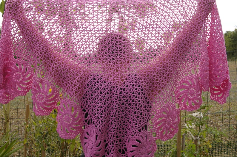 May include: A pink crocheted shawl with a delicate floral pattern. The shawl is draped over a person's shoulders, creating a soft and elegant look.