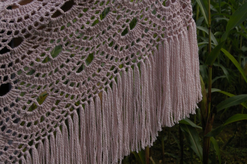 May include: A crocheted shawl with a delicate pattern and a fringe border. The shawl is a light pink color.
