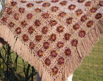 May include: A crocheted shawl with a fringe border in a light brown color. The shawl has a geometric pattern with colorful accents in shades of red, orange, and yellow.