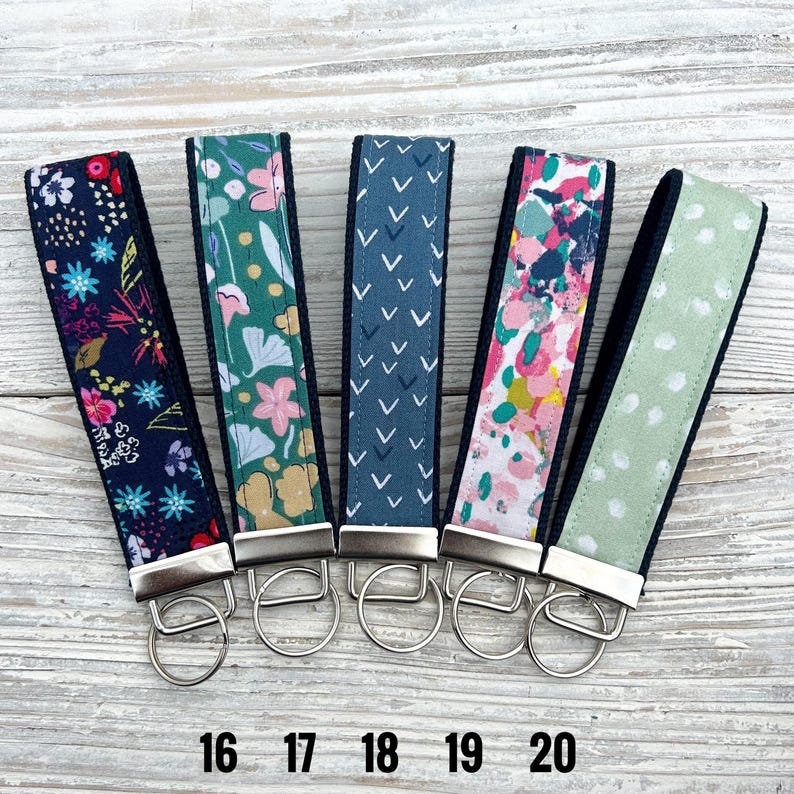 Peut inclure: Cinq porte-cl&eacute;s en tissu avec diff&eacute;rents motifs : floral marine, floral vert, chevrons marine, abstrait rose et vert, et pois vert clair. Chacun a une bordure noire et un porte-cl&eacute;s argent&eacute;. Les num&eacute;ros 16-20 sont imprim&eacute;s en dessous.