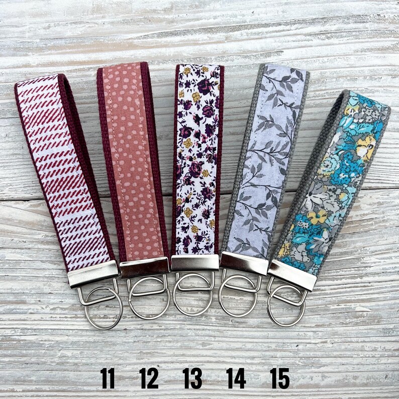 Peut inclure: Cinq porte-cl&eacute;s en tissu avec des accessoires argent&eacute;s. Les porte-cl&eacute;s pr&eacute;sentent divers motifs, dont un chevrons blanc et bordeaux, des pois roses, des motifs floraux, des feuilles grises et un motif floral bleu. Les num&eacute;ros 11, 12, 13, 14 et 15 sont imprim&eacute;s en bas.