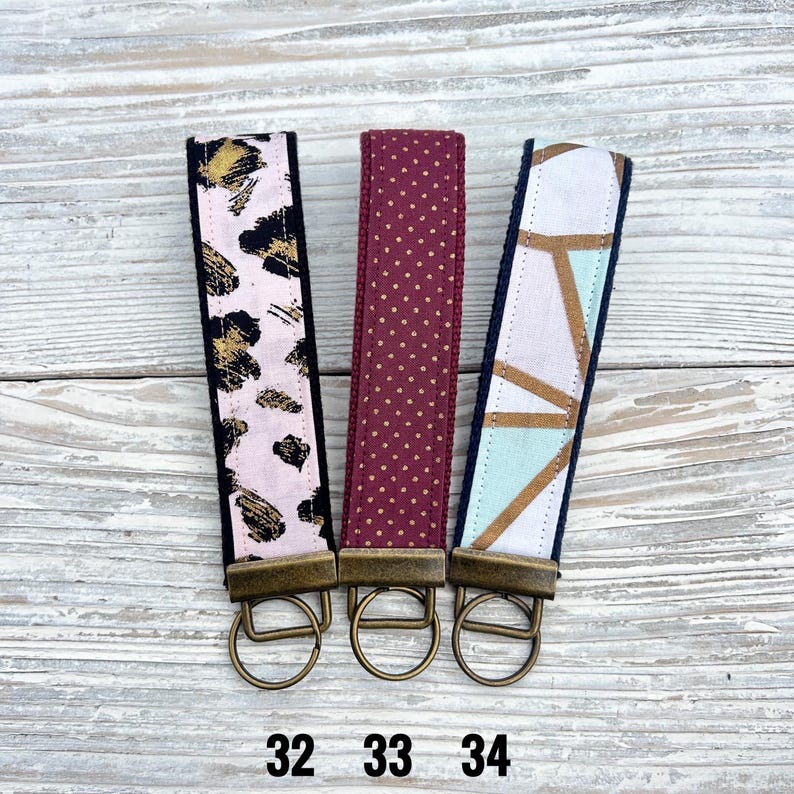 Peut inclure: Trois porte-cl&eacute;s avec diff&eacute;rents motifs. L'un pr&eacute;sente un fond rose avec un imprim&eacute; l&eacute;opard noir et or. Le second est bordeaux avec des pois dor&eacute;s. Le troisi&egrave;me a un design g&eacute;om&eacute;trique avec des formes dor&eacute;es, bleues et blanches. Chaque porte-cl&eacute;s a un anneau en m&eacute;tal de couleur bronze.
