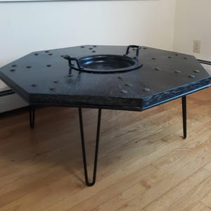 May include: Octagonal black wooden coffee table with a metal insert and hairpin legs. The table top is studded with metal accents.