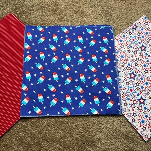 May include: Three fabric squares with different patterns. The first square is red with white polka dots. The second square is blue with white stars and red and white popsicle designs. The third square is white with red and blue stars.