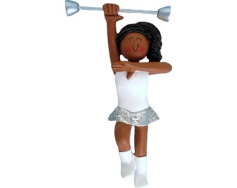 May include: A figurine of a person twirling a baton. The figure is wearing a white leotard with a silver sequined skirt and white boots. The baton is silver with silver ends. The figure has dark skin and black hair.