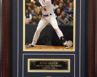 May include: Framed photo of baseball player Ryan Braun of the Milwaukee Brewers. The image shows Braun in a batting stance, with a baseball in the foreground. The frame includes a nameplate and the number 8.