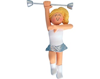 May include: A figurine of a blonde baton twirler in a white leotard with a silver sequined skirt and white boots. The twirler is holding a silver baton above their head.
