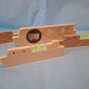 May include: Wooden spirit levels and bottle opener combination tools. The levels have a clear vial with a green liquid bubble. One level has a built-in bottle opener. The wood is light and medium brown.