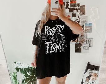 May include: A black t-shirt with the text "Rizz 'em with the Tism" in white, paired with an orange baseball cap. The cap features the text "I AM LOVE FOR LOVE" in white. The outfit is completed with white cowboy boots.