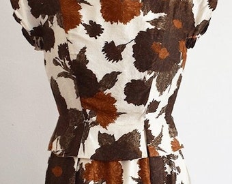 May include: A white dress with a brown and orange floral print. The dress has a fitted bodice and a full skirt. The dress is sleeveless and has a scoop neckline.
