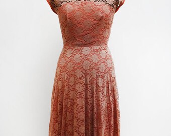 May include: A vintage-style, coral-colored lace dress with a fitted bodice and a full skirt. The dress has a round neckline and short sleeves.