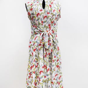 May include: A sleeveless white dress with a floral pattern of red, green, and blue accents. The dress features a keyhole back and a tie-waist design. The dress is displayed on a mannequin.