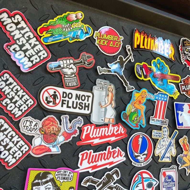 Pu&ograve; includere: Una collezione di adesivi colorati con vari disegni, tra cui un mostro, un idraulico, un martello, un water, una creatura della laguna nera e un logo dei Grateful Dead. Gli adesivi sono su uno sfondo nero e argento.