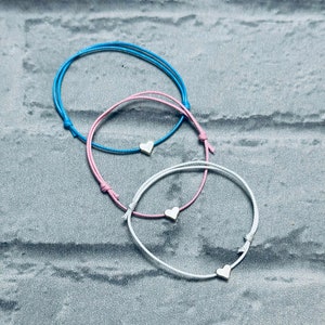 Puede incluir: Tres pulseras de la amistad con dijes en forma de corazón. Las pulseras son azules, rosas y blancas.