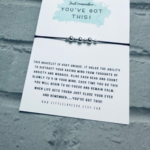 May include: A black string bracelet with silver beads. The bracelet is accompanied by a card with the text "Just remember... YOU'VE GOT THIS!" and instructions on how to use the bracelet as a mindfulness tool. The card also includes the website address "www.littlelovesxo.etsy.com".