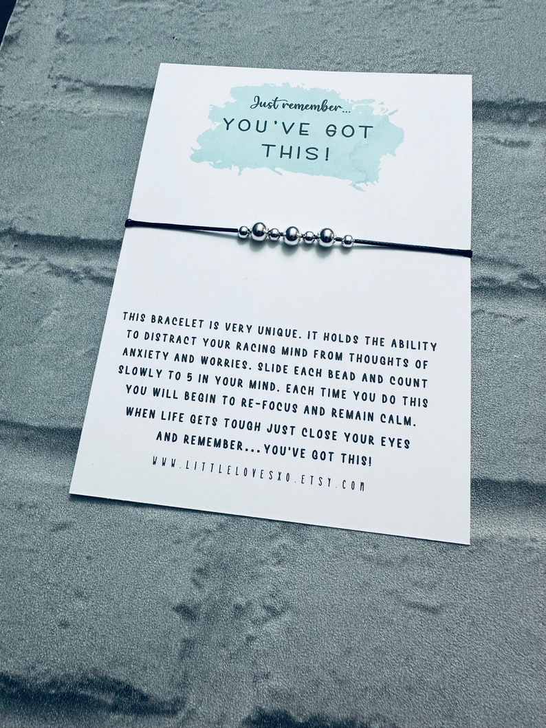 May include: A black string bracelet with silver beads. The bracelet is accompanied by a card with the text "Just remember... YOU'VE GOT THIS!" and instructions on how to use the bracelet as a mindfulness tool. The card also includes the website address "www.littlelovesxo.etsy.com".