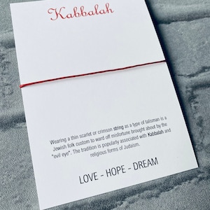 Pode incluir: Pulseira de corda vermelha com a palavra "Kabbalah" e o texto "Usar um fio fino escarlate ou carmesim como um tipo de talism&atilde; &eacute; um costume popular judeu para evitar a m&aacute; sorte causada pelo "mau-olhado". A tradi&ccedil;&atilde;o &eacute; popularmente associada &agrave; Cabala e &agrave;s formas religiosas do juda&iacute;smo. LOVE - HOPE - DREAM"