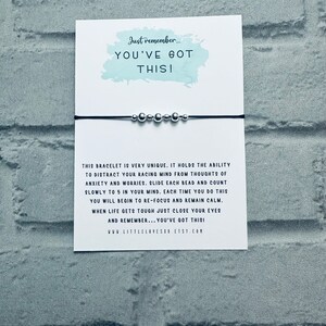 May include: A black string bracelet with silver beads. The bracelet is accompanied by a card with the text "Just remember... YOU'VE GOT THIS!" and a message about using the beads to focus and calm the mind.