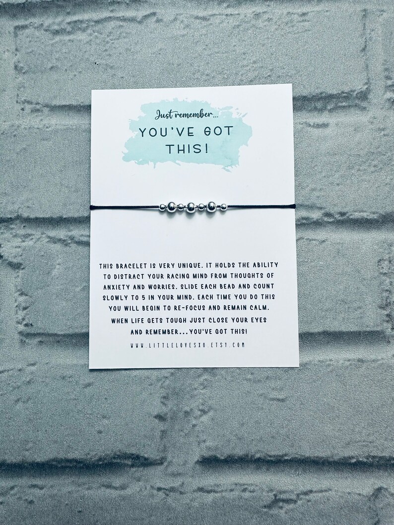 May include: A black string bracelet with silver beads. The bracelet is accompanied by a card with the text "Just remember... YOU'VE GOT THIS!" and a message about using the beads to focus and calm the mind.
