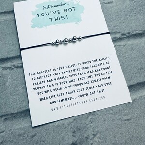 May include: A black string bracelet with silver beads. The bracelet is accompanied by a card with the text "Just remember... YOU'VE GOT THIS!" and a message about the bracelet's ability to help with anxiety and worries.