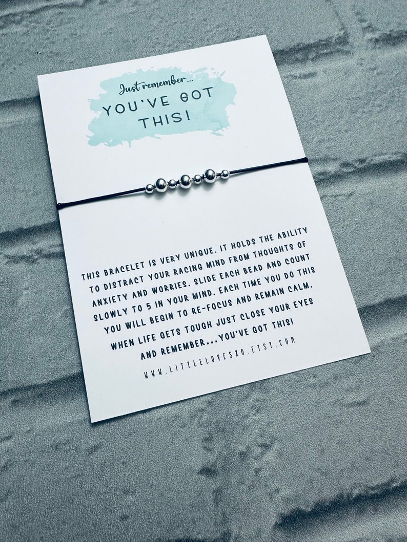 May include: A black string bracelet with silver beads. The bracelet is accompanied by a card with the text "Just remember... YOU'VE GOT THIS!" and a message about the bracelet's ability to help with anxiety and worries.