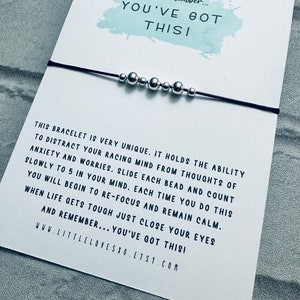 May include: A black string bracelet with silver beads. The bracelet comes with a card that reads "Just remember... YOU'VE GOT THIS!" and includes instructions on how to use the bracelet to help with anxiety and worries.