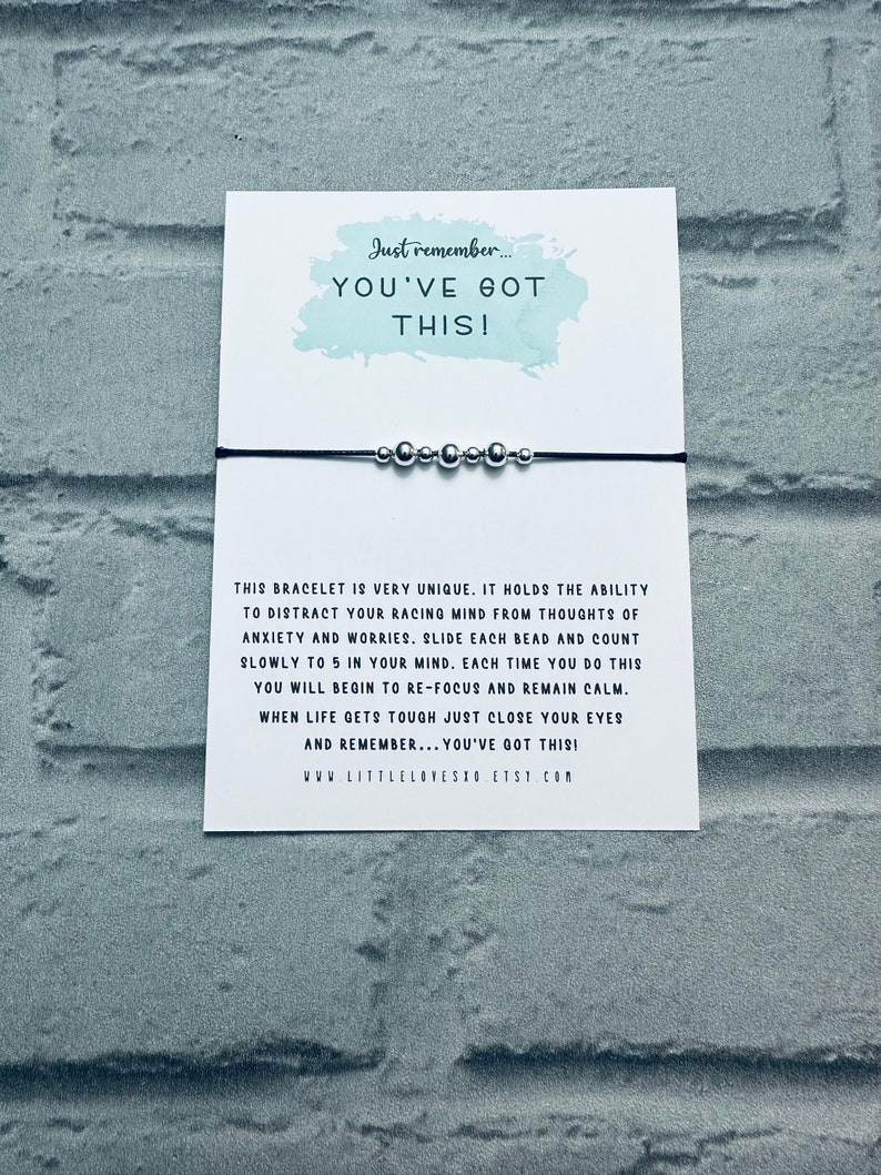 May include: A black string bracelet with silver beads. The bracelet is accompanied by a card with the text "Just remember... YOU'VE GOT THIS!" and instructions on how to use the bracelet as a mindfulness tool.