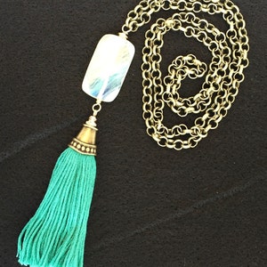 May include: A long gold chain necklace with a large iridescent rectangular pendant and a teal tassel.