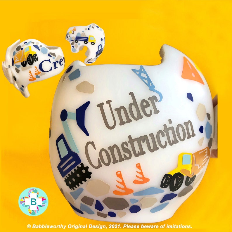 May include: White helmet with a blue and yellow construction theme. The helmet has the words "Under Construction" written on it.