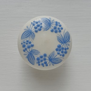 May include: White ceramic knob with a blue and white floral design. The design features a wreath of blue leaves and berries.