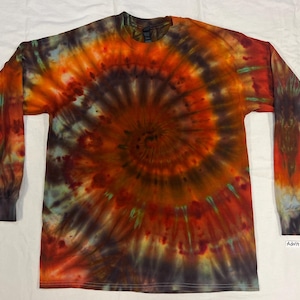 May include: A long-sleeve crew neck t-shirt featuring a spiral tie-dye pattern in shades of orange, brown, black, and hints of teal. The shirt has a label on the bottom right corner that reads Adult Large.