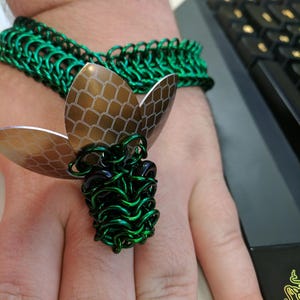 May include: A green metal bracelet with a matching ring. The ring has a decorative design with brown scales.