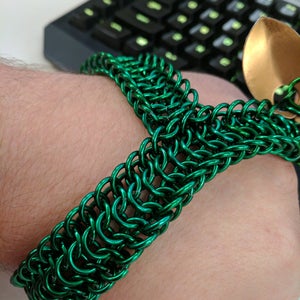 May include: A green metal chainmail bracelet. The bracelet is made of small, interconnected metal rings.