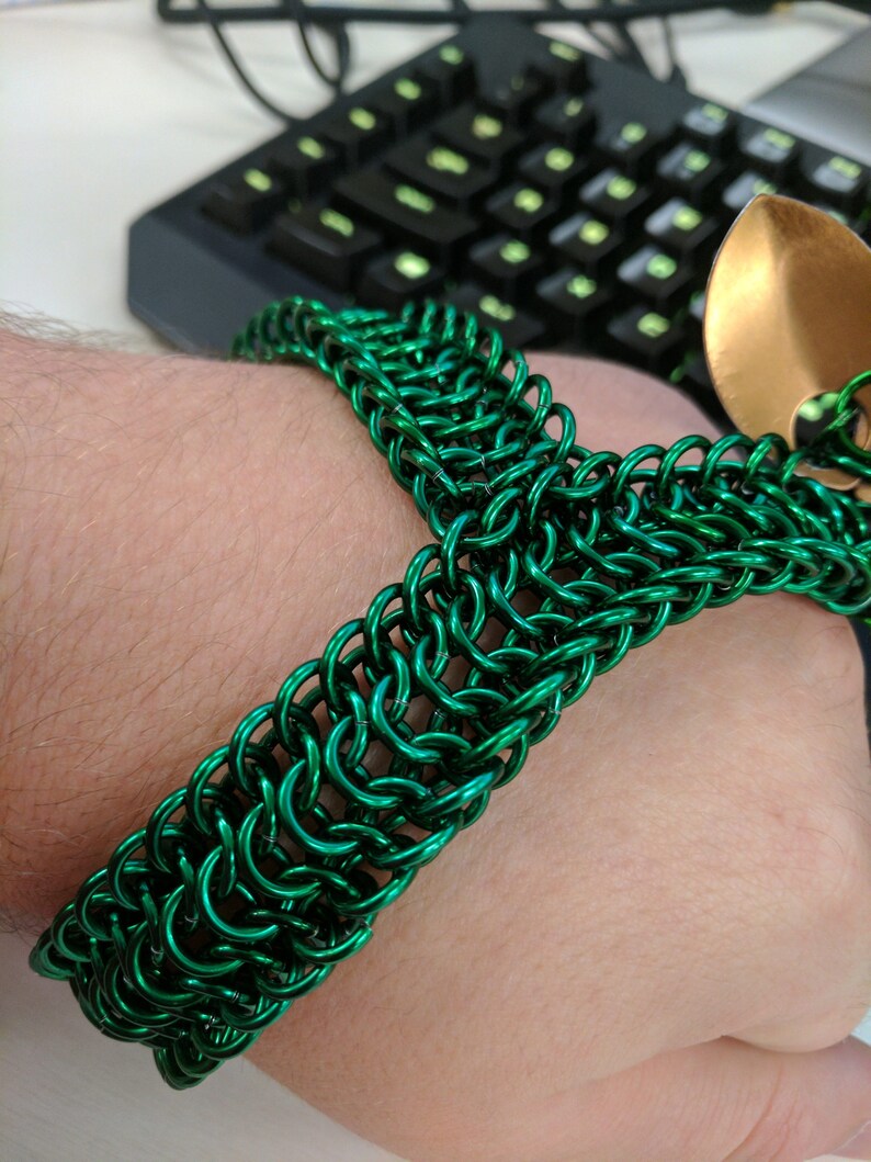 May include: A green metal chainmail bracelet. The bracelet is made of small, interconnected metal rings.