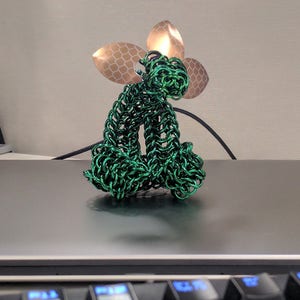 May include: A green wire sculpture of a sitting animal with a gold leaf design on its head.