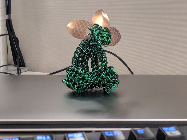 May include: A green wire sculpture of a sitting animal with a gold leaf design on its head.