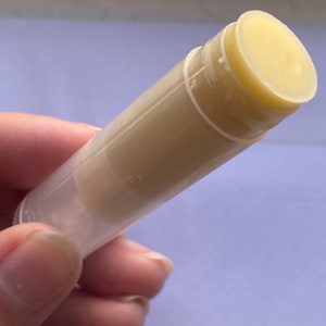 May include: A clear plastic tube with a white lip balm inside. The balm is visible through the tube.