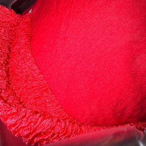 May include: A bright red bra with a smooth, solid cup and a textured, fringed edge. The bra appears to be made of a soft fabric, and the image is a close-up, highlighting the details of the garment.