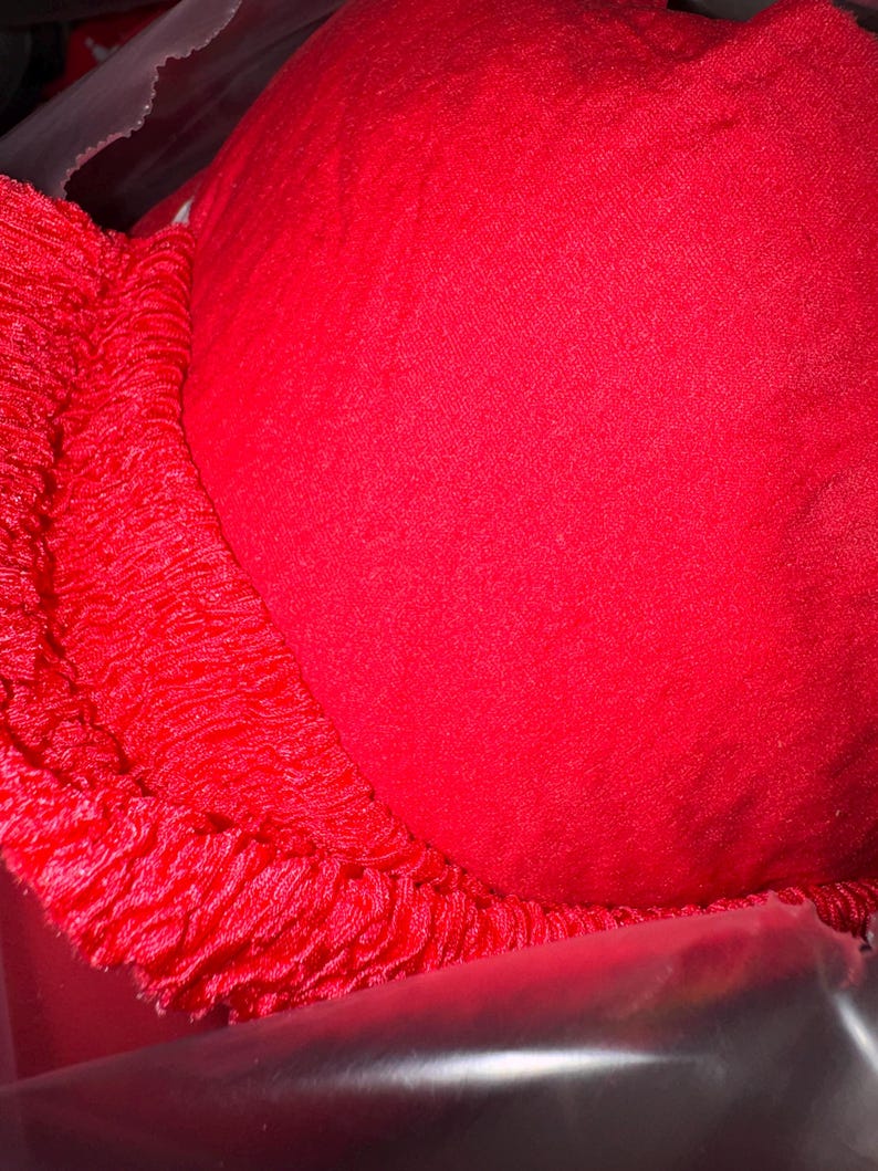 May include: A bright red bra with a smooth, solid cup and a textured, fringed edge. The bra appears to be made of a soft fabric, and the image is a close-up, highlighting the details of the garment.