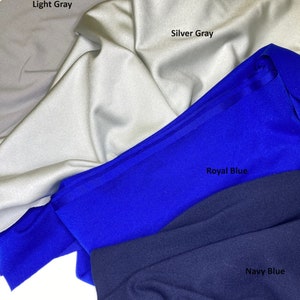 May include: Close-up of fabric swatches in light gray, silver gray, royal blue, and navy blue. The fabric is folded and draped, with the names of the colors printed on the fabric. The fabric appears to be a smooth, possibly synthetic material.