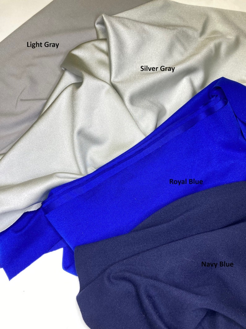 May include: Close-up of fabric swatches in light gray, silver gray, royal blue, and navy blue. The fabric is folded and draped, with the names of the colors printed on the fabric. The fabric appears to be a smooth, possibly synthetic material.