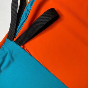 May include: A turquoise and orange fabric bag with black straps. The bag has a simple design and is made of a durable material.