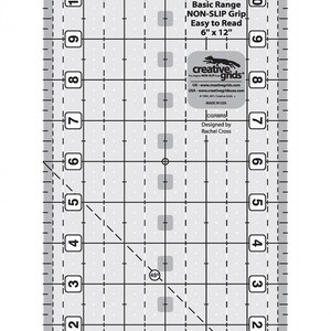 May include: A 6-inch by 12-inch clear ruler with a grid pattern and a 45-degree angle line. The ruler has a non-slip grip and is easy to read. It is labeled "Basic Range Non-Slip Grip Easy to Read 6" x 12" Creative Grids".
