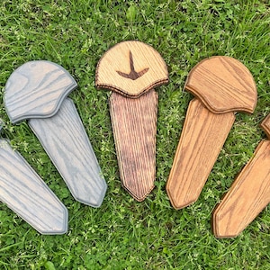 May include: Five wooden decorative pieces with a bird-like design, arranged on green grass. The pieces vary in color, including gray, light brown, and dark brown. Each piece has a unique wood grain pattern and a carved bird graphic.