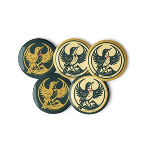 May include: A collection of five round buttons featuring a bird design. The birds are depicted with outstretched wings and a red heart on their chest. The buttons have a dark green and gold color scheme, with the text "THREE BUDS.COM" at the bottom.