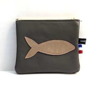 May include: A dark grey rectangular zipped pouch featuring a beige fish-shaped appliqué centred on the front. A small black fabric tag on the side displays the text 100% above a small blue, white, and red striped flag detail.