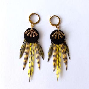 May include: A pair of gold hoop earrings with black leather and gold accents. Each earring features a cluster of yellow and black feathers.