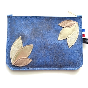 Könnte beinhalten: Eine blaue Reißverschlusstasche mit goldenen und beigefarbenen Blättern. Die Tasche hat eine strukturierte Oberfläche und einen goldfarbenen Reißverschluss. Ein kleines Etikett mit dem Text "100%" und einer französischen Flagge ist angebracht.